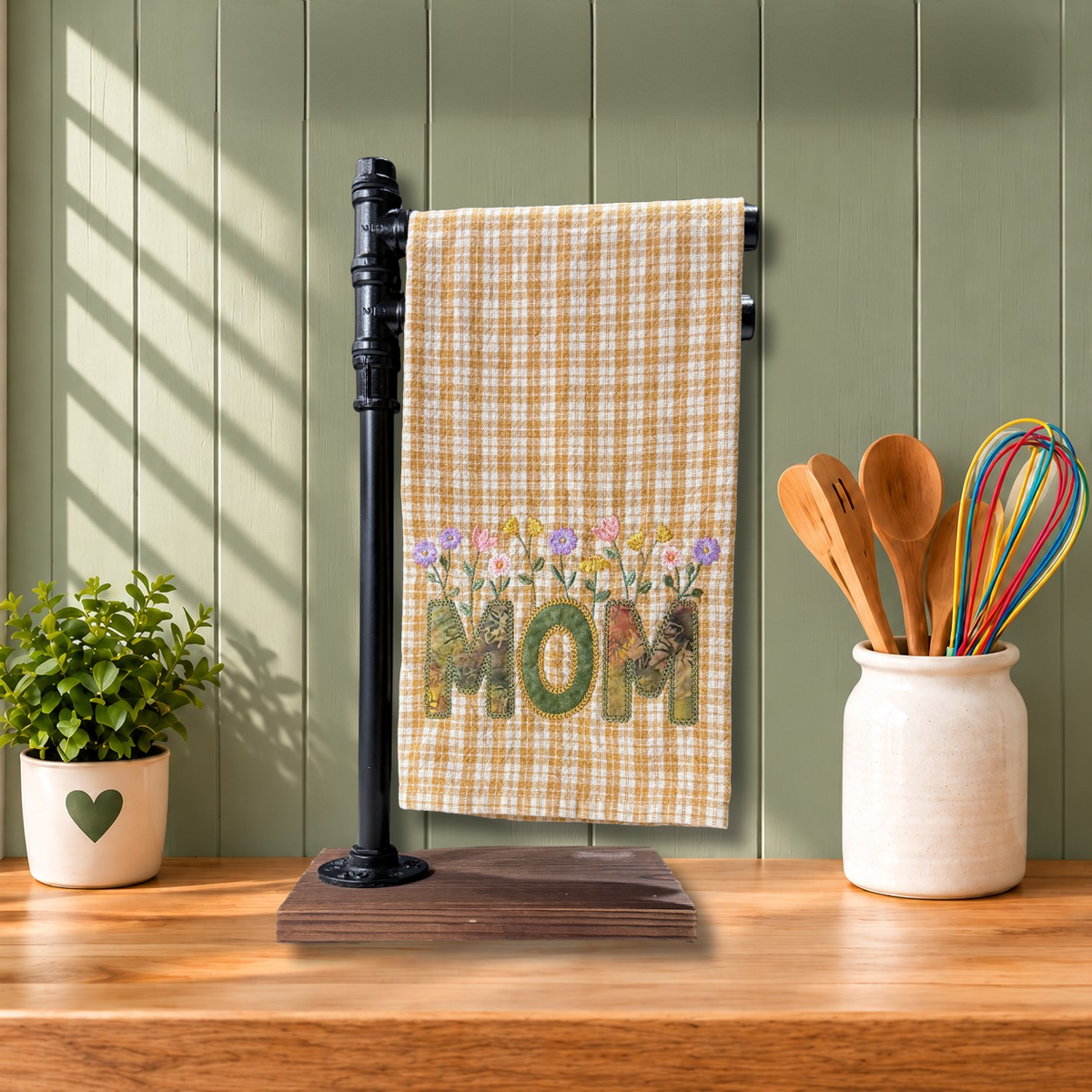 A kitchen towel with a Golden yellow gingham pattern and a colorful floral design spelling 'MOM'.